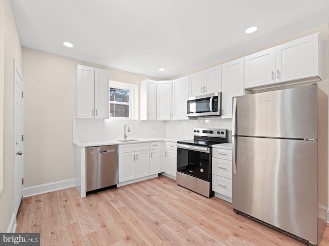 kitchen with white cabinets, sink, light hardwood / wood-style flooring, tasteful backsplash, and stainless steel appliances