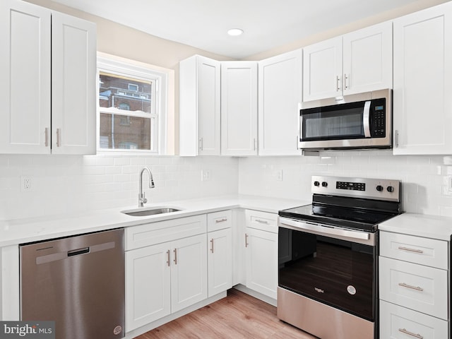 kitchen with decorative backsplash, stainless steel appliances, sink, light hardwood / wood-style flooring, and white cabinetry