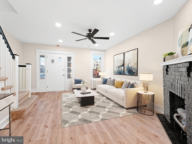 living room featuring ceiling fan, light wood-type flooring, a wealth of natural light, and a brick fireplace