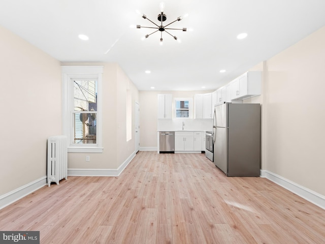 kitchen with light wood-type flooring, radiator, stainless steel appliances, sink, and white cabinets