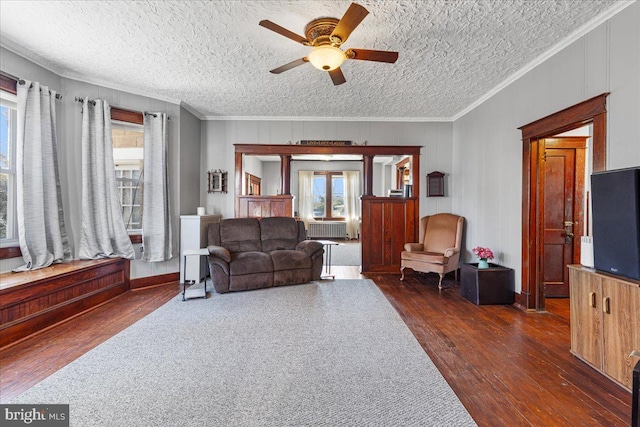 living room with a textured ceiling, ceiling fan, ornamental molding, and dark wood-type flooring