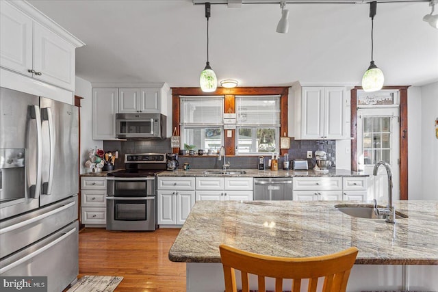 kitchen with decorative light fixtures, sink, white cabinetry, and stainless steel appliances