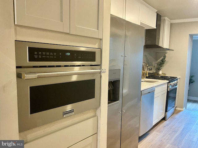 kitchen with white cabinetry, wall chimney range hood, backsplash, light hardwood / wood-style floors, and appliances with stainless steel finishes