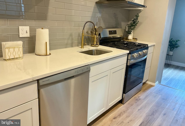 kitchen featuring light wood-type flooring, stainless steel appliances, sink, white cabinetry, and range hood