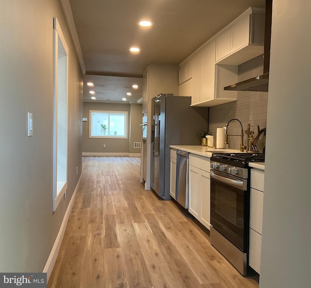 kitchen featuring light wood-type flooring, tasteful backsplash, ornamental molding, stainless steel appliances, and white cabinetry