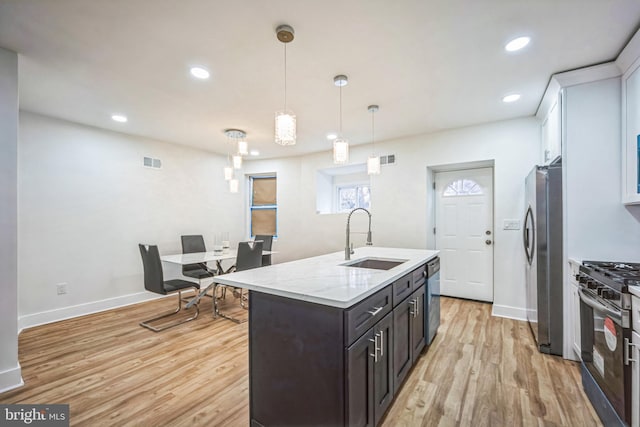 kitchen with sink, hanging light fixtures, light hardwood / wood-style flooring, an island with sink, and stainless steel appliances