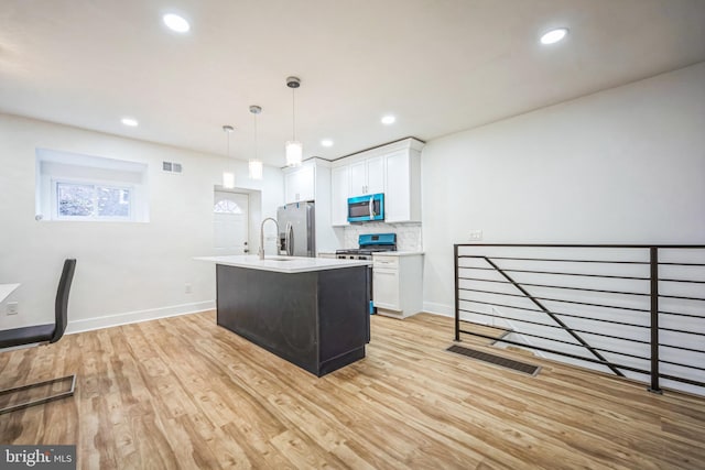 kitchen featuring stainless steel appliances, a kitchen island with sink, light hardwood / wood-style flooring, white cabinets, and hanging light fixtures