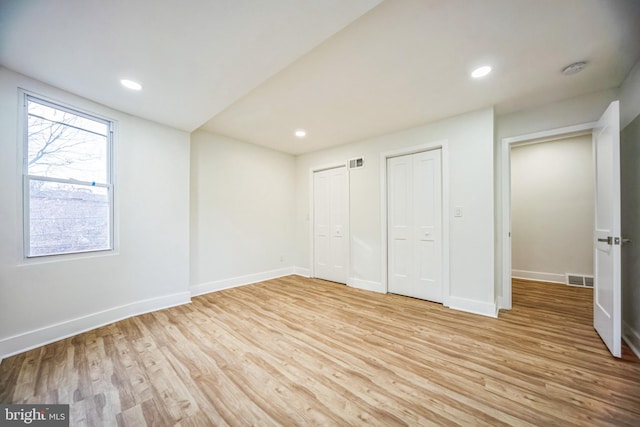 unfurnished bedroom featuring light hardwood / wood-style floors and two closets