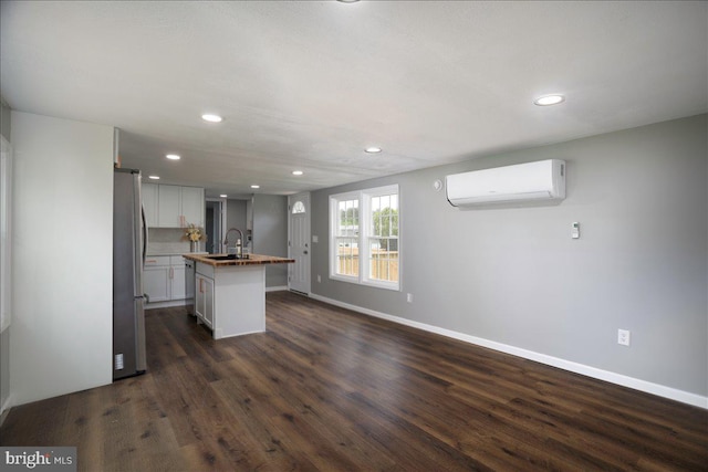 kitchen with white cabinets, an AC wall unit, sink, an island with sink, and dark hardwood / wood-style flooring