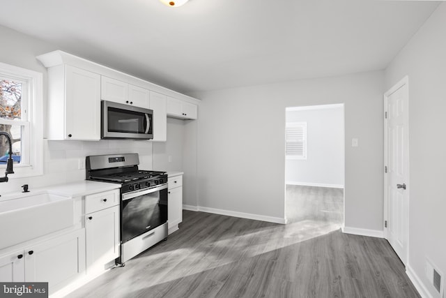 kitchen featuring white cabinetry, sink, stainless steel appliances, tasteful backsplash, and light wood-type flooring