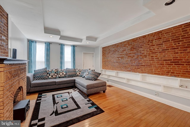 living room with light hardwood / wood-style floors, brick wall, and a tray ceiling