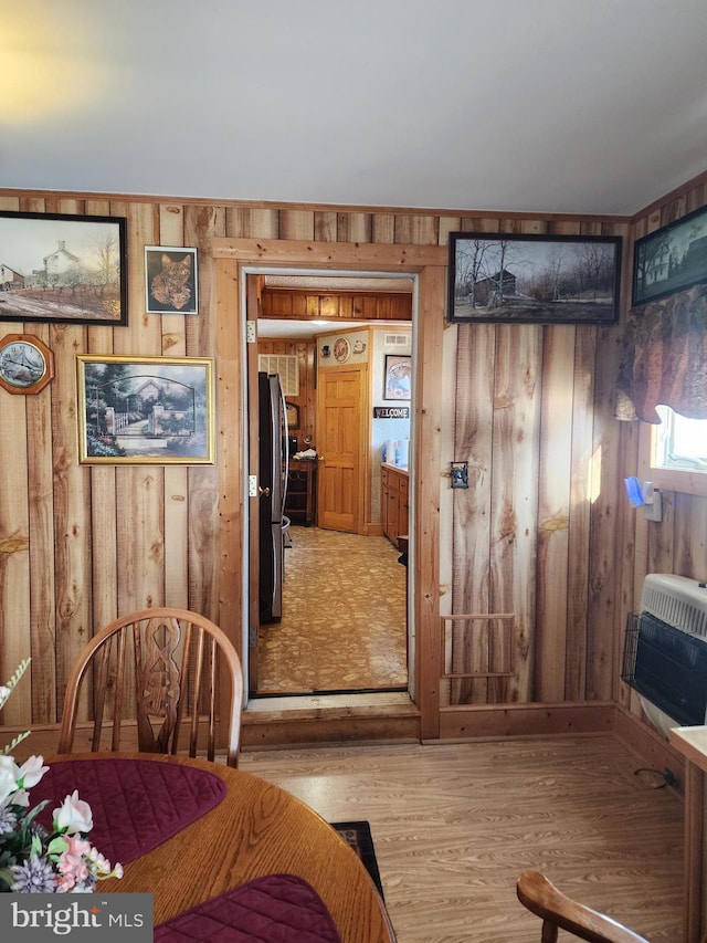 bedroom featuring stainless steel fridge, light hardwood / wood-style floors, wooden walls, and heating unit