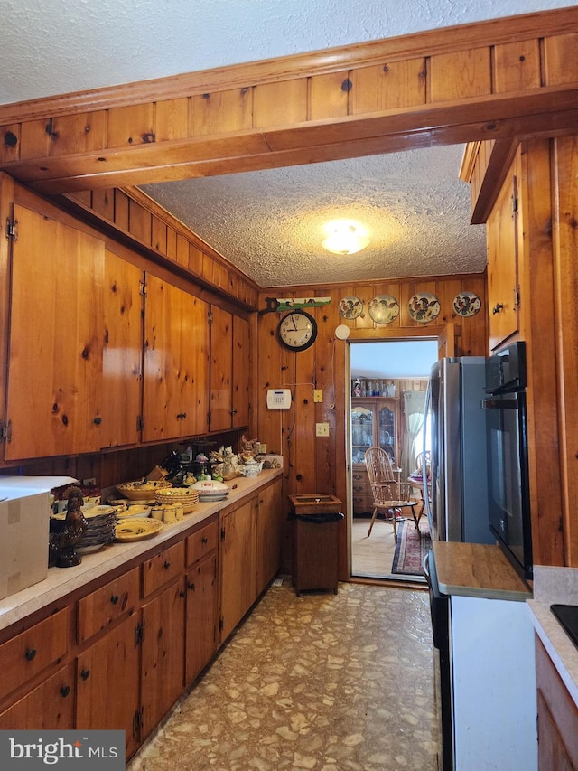 kitchen with stainless steel fridge, black oven, wooden walls, and a textured ceiling