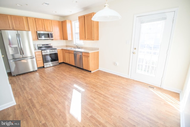 kitchen featuring sink, stainless steel appliances, hanging light fixtures, and light hardwood / wood-style floors