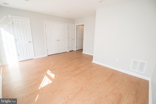 unfurnished bedroom featuring light hardwood / wood-style floors and two closets