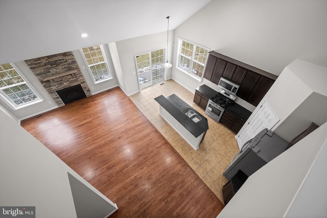 living room featuring a stone fireplace, high vaulted ceiling, and light hardwood / wood-style flooring