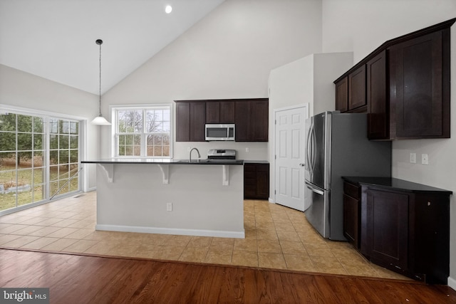 kitchen with light hardwood / wood-style flooring, high vaulted ceiling, decorative light fixtures, a center island with sink, and appliances with stainless steel finishes