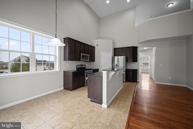 kitchen featuring hanging light fixtures, high vaulted ceiling, an island with sink, appliances with stainless steel finishes, and light wood-type flooring