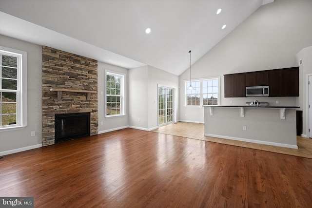 unfurnished living room featuring a fireplace, light hardwood / wood-style floors, high vaulted ceiling, and plenty of natural light