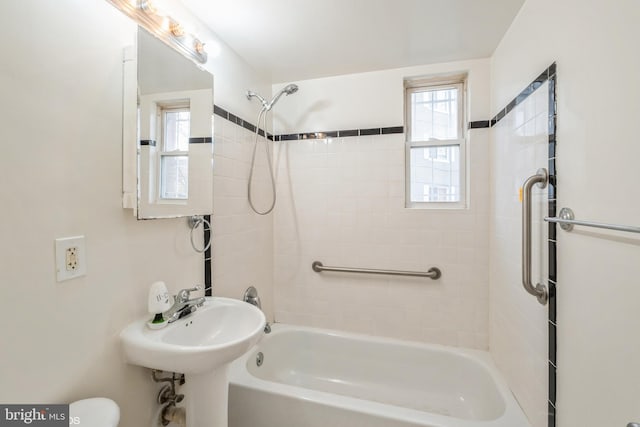 bathroom with tiled shower / bath combo, plenty of natural light, and sink