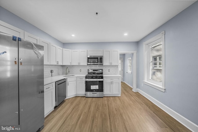 kitchen with backsplash, light wood-type flooring, stainless steel appliances, sink, and white cabinetry