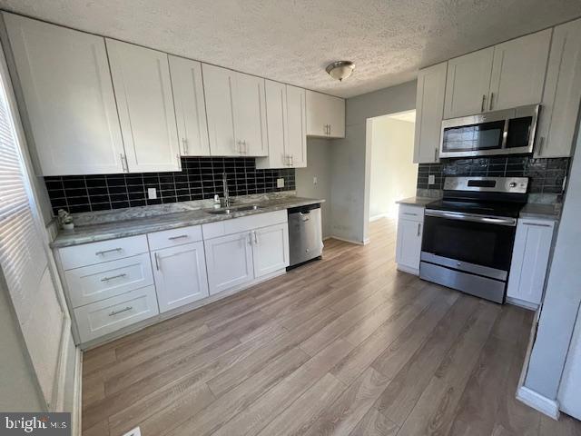 kitchen featuring white cabinetry, sink, stainless steel appliances, light hardwood / wood-style floors, and decorative backsplash