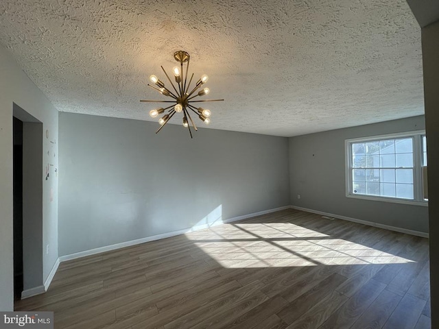 spare room with hardwood / wood-style floors, a chandelier, and a textured ceiling