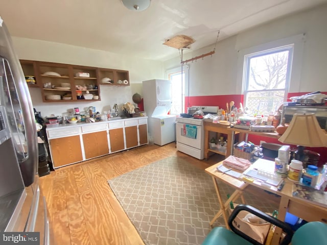 kitchen featuring white range, light hardwood / wood-style floors, stainless steel refrigerator, and stacked washer / drying machine