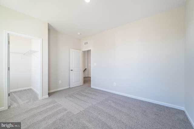 unfurnished bedroom with a spacious closet, light carpet, and a closet