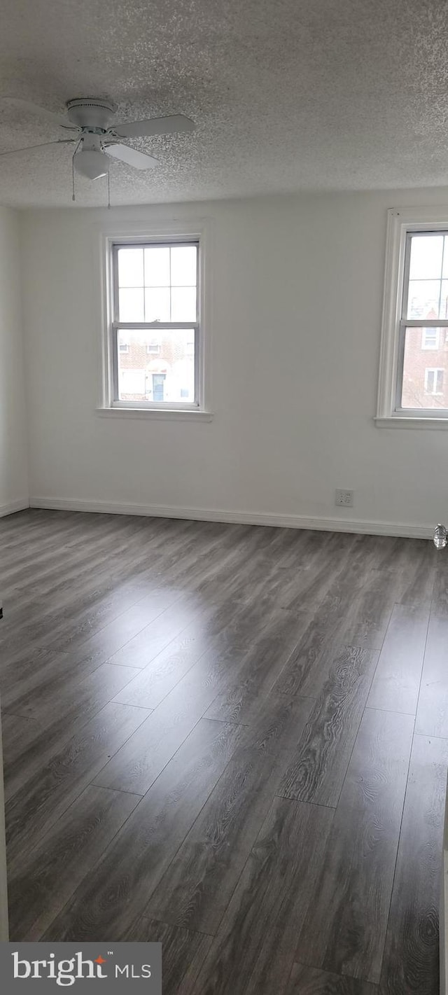 spare room featuring a textured ceiling, ceiling fan, dark wood finished floors, and baseboards