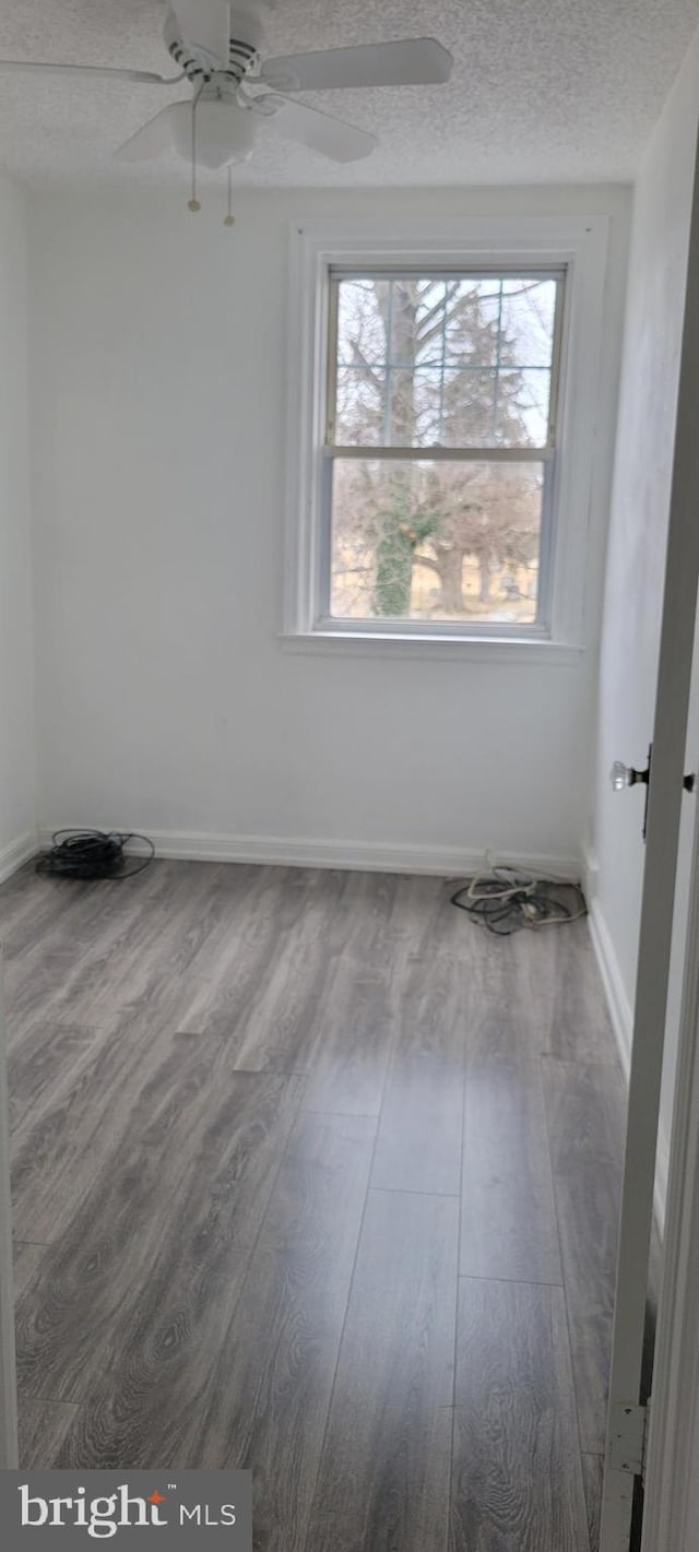 unfurnished room featuring ceiling fan, a textured ceiling, baseboards, and wood finished floors