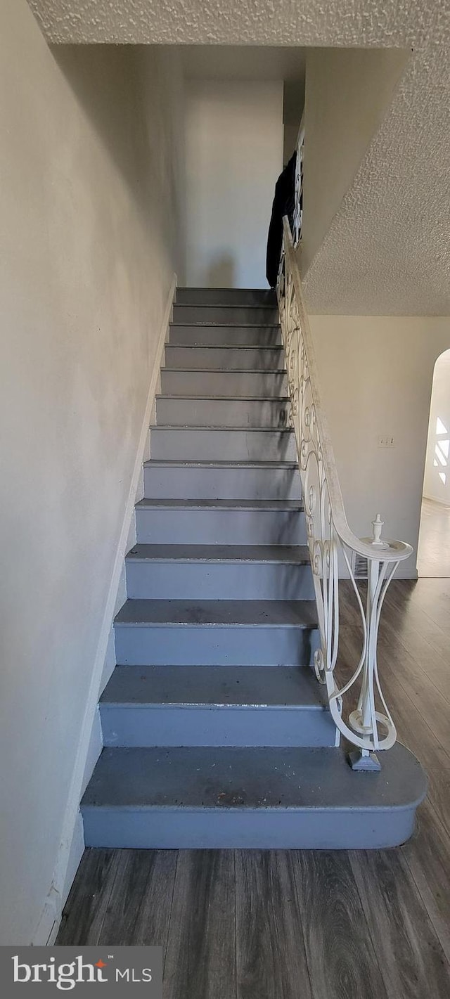 stairway featuring baseboards, a textured ceiling, arched walkways, and wood finished floors