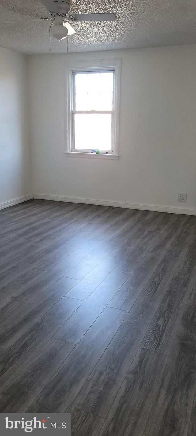 spare room featuring dark wood-type flooring, a textured ceiling, and baseboards