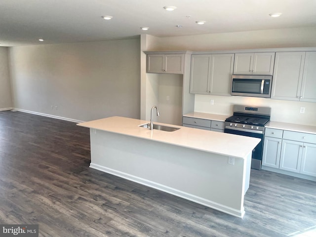 kitchen with a center island with sink, sink, appliances with stainless steel finishes, and dark wood-type flooring