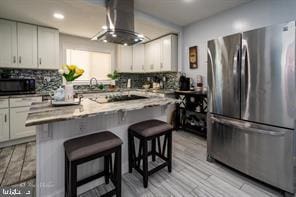 kitchen with exhaust hood, stainless steel fridge, black electric stovetop, white cabinets, and a breakfast bar