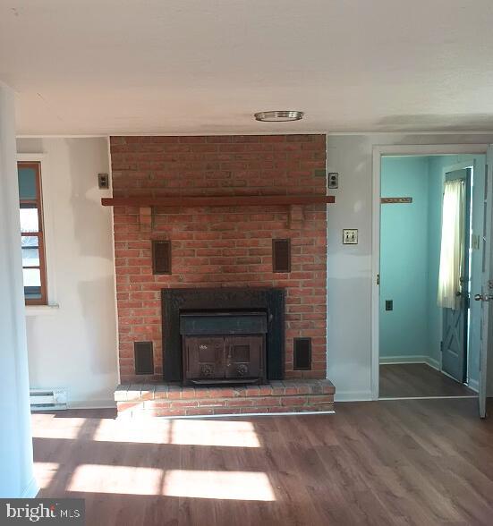 unfurnished living room featuring hardwood / wood-style floors, a healthy amount of sunlight, a fireplace, and a baseboard radiator