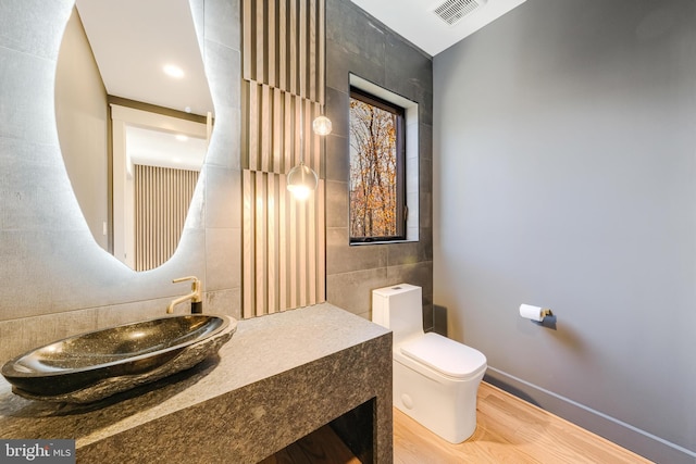 bathroom featuring toilet, sink, wood-type flooring, and tile walls