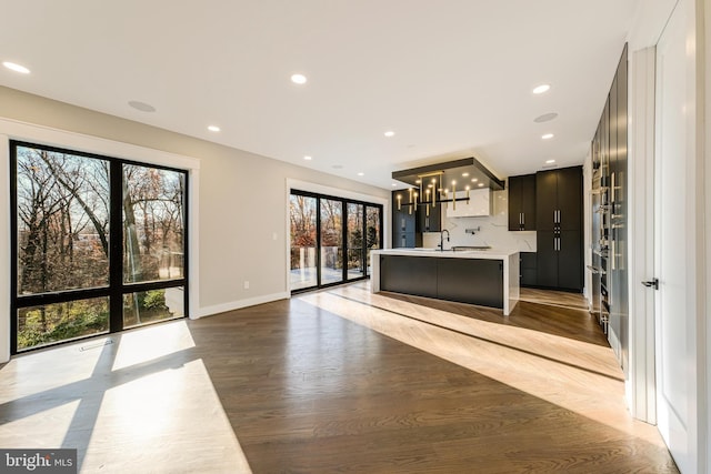 kitchen with sink, tasteful backsplash, dark hardwood / wood-style flooring, a chandelier, and a kitchen island with sink