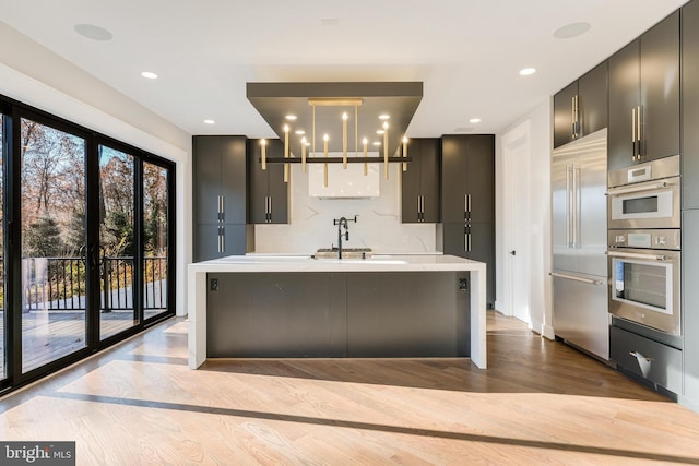 kitchen featuring sink, stainless steel appliances, backsplash, light hardwood / wood-style floors, and decorative light fixtures