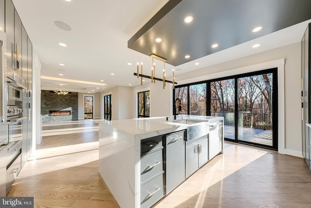 kitchen with sink, a stone fireplace, stainless steel dishwasher, pendant lighting, and light wood-type flooring