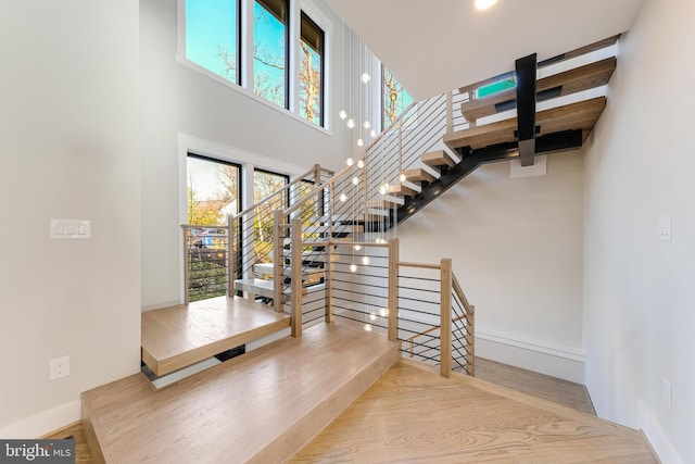 stairway with hardwood / wood-style floors, a towering ceiling, and a healthy amount of sunlight