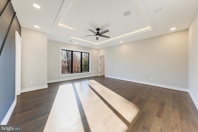 empty room with dark hardwood / wood-style flooring, a tray ceiling, and ceiling fan