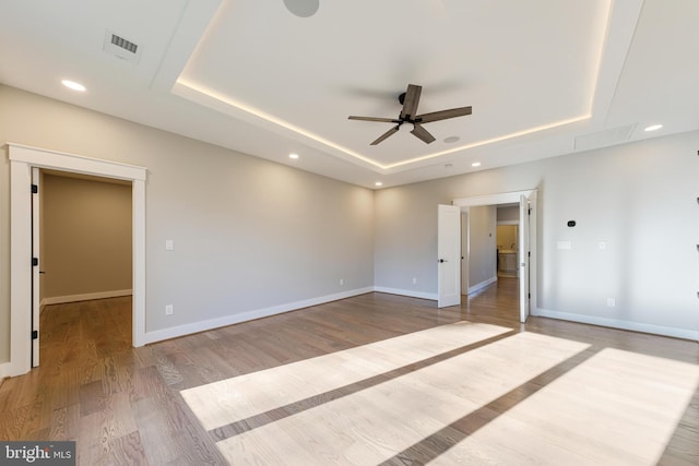 spare room with light wood-type flooring, a raised ceiling, and ceiling fan