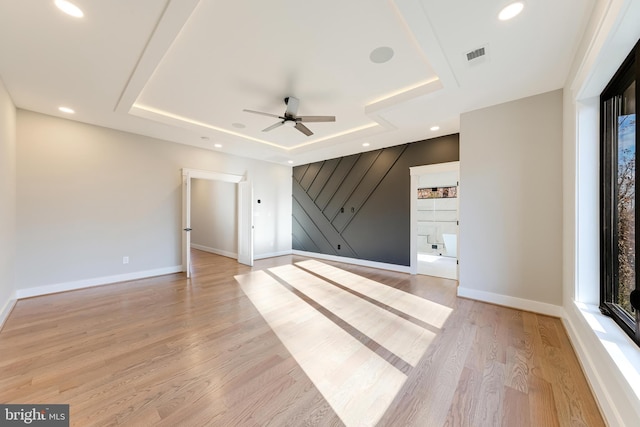 spare room with a raised ceiling, ceiling fan, and light hardwood / wood-style floors