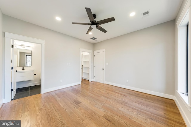 unfurnished bedroom with light hardwood / wood-style floors, a walk in closet, connected bathroom, and multiple windows