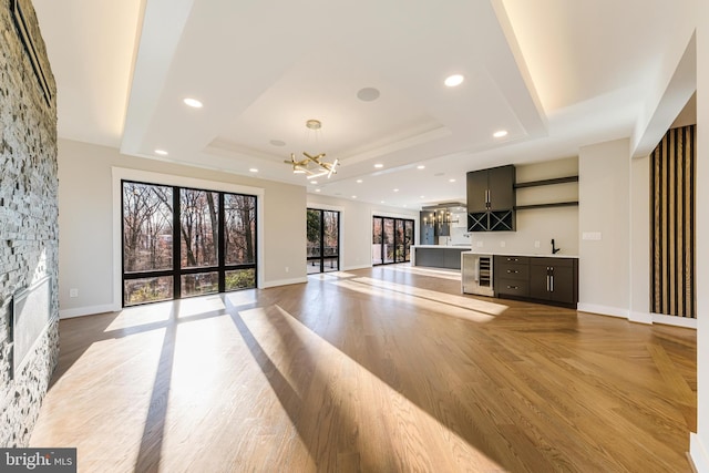 unfurnished living room with a chandelier, a stone fireplace, light hardwood / wood-style flooring, and a tray ceiling