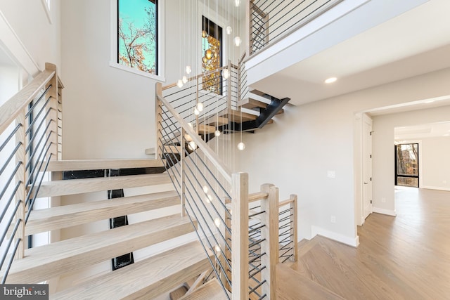 stairs featuring wood-type flooring, a towering ceiling, and a healthy amount of sunlight