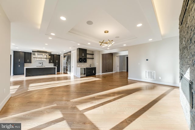 unfurnished living room with a fireplace, light wood-type flooring, a raised ceiling, and a notable chandelier