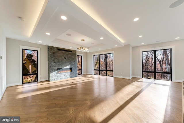 unfurnished living room featuring plenty of natural light, light hardwood / wood-style floors, a fireplace, and a tray ceiling