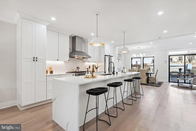 kitchen with white cabinets, light hardwood / wood-style floors, wall chimney range hood, and a kitchen island with sink